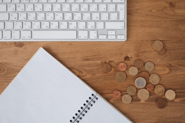 Caiet cu un buget lunar scris de mână, un calculator și câteva monede pe biroul unui student