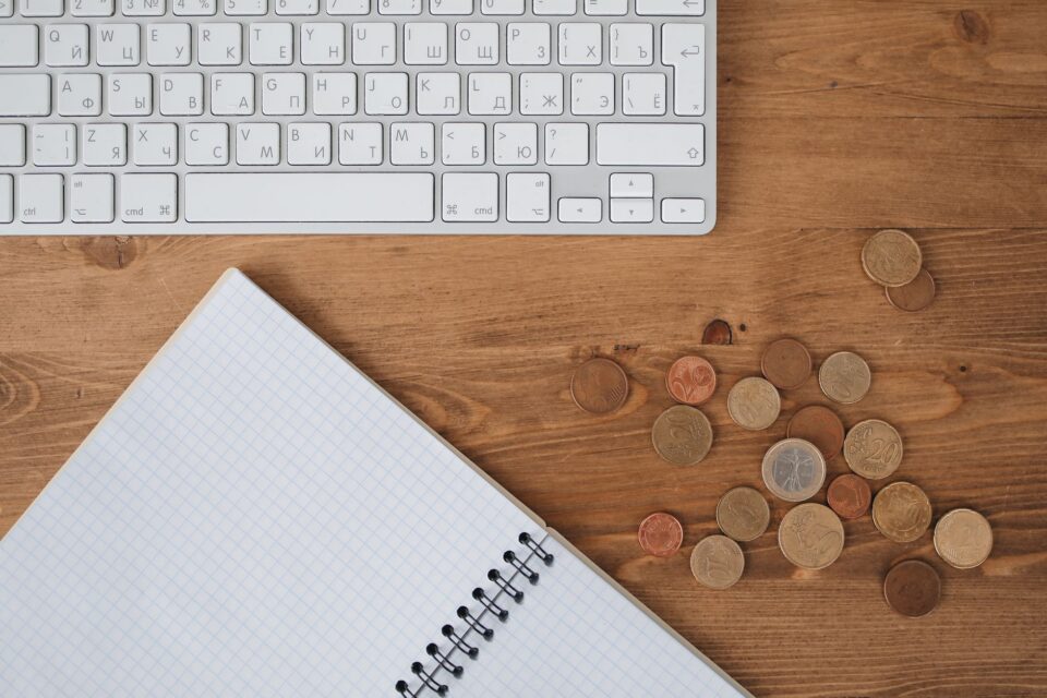Caiet cu un buget lunar scris de mână, un calculator și câteva monede pe biroul unui student