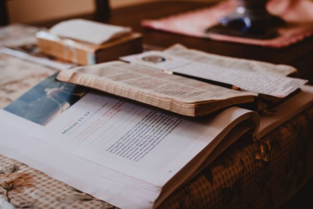 Cărți deschise, fișe cu notițe și un laptop pe o masă din biblioteca universității