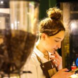 Student care lucrează part-time ca barista într-o cafenea, pregătind o cafea pentru un client